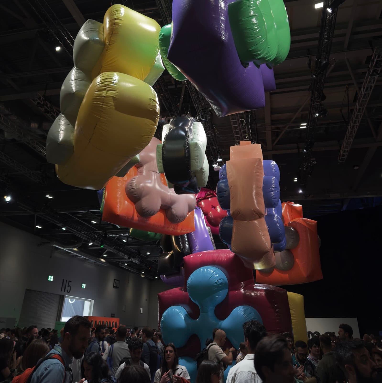 Giant inflatable Config letterforms in yellow, purple, pink and blue hanging over the crowd in the exhibition hall