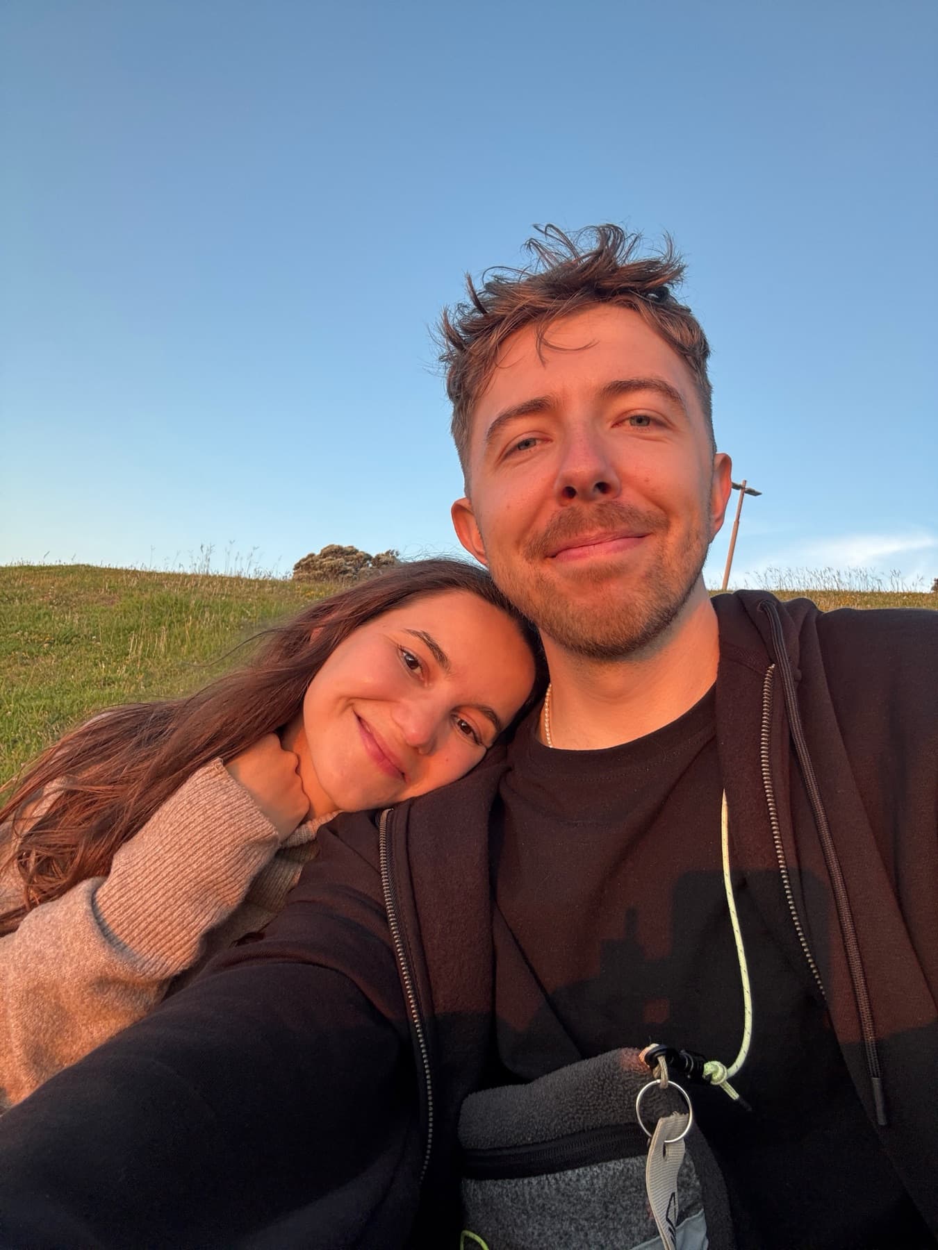 A selfie with someone on a grassy hillside at golden hour