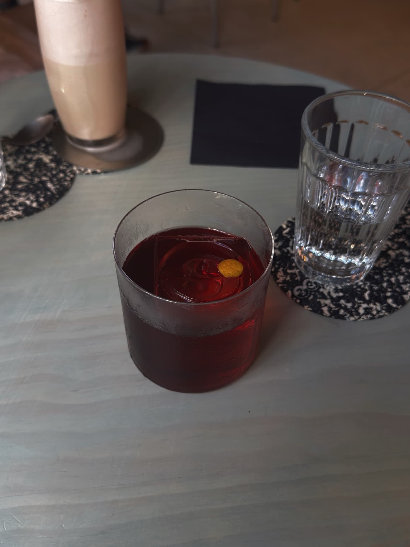 A dark red cocktail on a table, a glass of water beside it