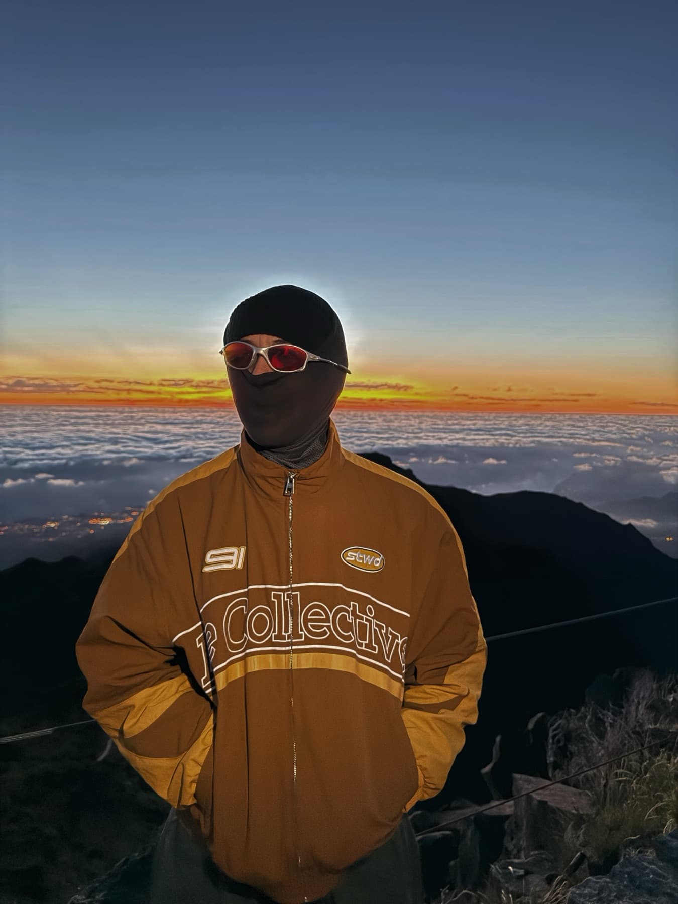 In a balaclava and sunglasses on a summit above the clouds at sunrise